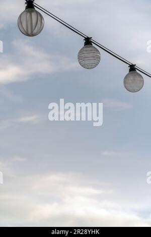 Three light bulbs on string wire against cloudy sky background Stock Photo