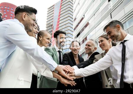 Group of smiling multiethnic businessman and businesswoman holding hands together outside. Multiracial cheerful successful executive team standing in Stock Photo