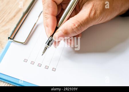 Close- up, Men's fingers holding pen writing on checklist paper and the format for filling in information in business concept. Businessman writing on Stock Photo