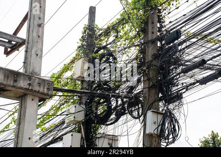 Electricity and cables, internet, and surveillance cameras were neatly installed on poles. Many wires are entangled. The vines on electric lines and c Stock Photo