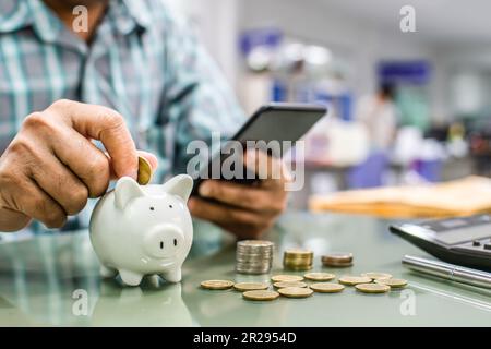 Businessman with coin and putting a piggy bank. White piggy bank many calculators and coins are placed on a desk at the office. Concept of saving mone Stock Photo