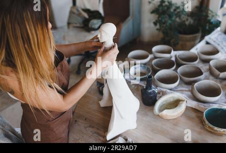 A young woman works in her pottery workshop. Pottery work. Creation of clay products. Stock Photo