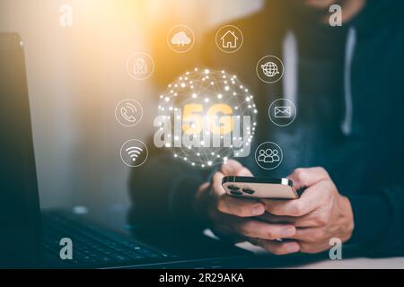 Man hold smartphone with Global network connection 5G virtual interface screen on laptop device, 5G mobile concept, technology network wireless system Stock Photo