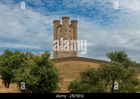 Low angle view of Broadway Tower on top of Beacon hill along the route of the Cotswold Way in England with trees and limestone dry-stone wall in front Stock Photo