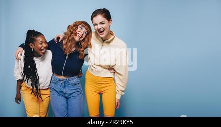 Multiethnic young women laughing and having fun while embracing each other. Group of cheerful female friends enjoying themselves while standing agains Stock Photo