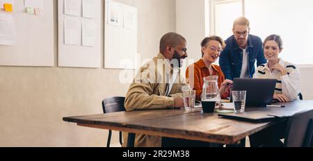 Cheerful business colleagues watching a slideshow presentation of their work during an office meeting. Group of happy interior designers working toget Stock Photo