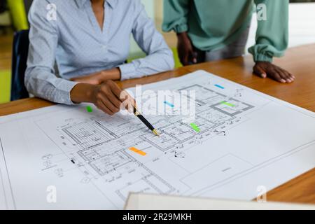 Midsection of african american female architects analyzing blueprint on desk in office, copy space Stock Photo