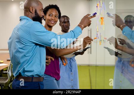 African american male and female colleagues discussing over adhesive notes on glass wall in office Stock Photo