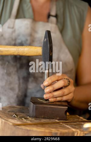 Midsection of caucasian female worker making jewellery using hammer at jewellery workshop Stock Photo