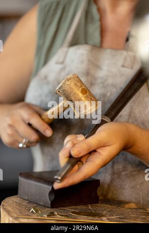 Midsection of caucasian female worker making jewellery using hammer at jewellery workshop Stock Photo