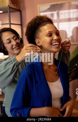 Diverse female jeweller and customers trying on necklace at jewellery shop Stock Photo