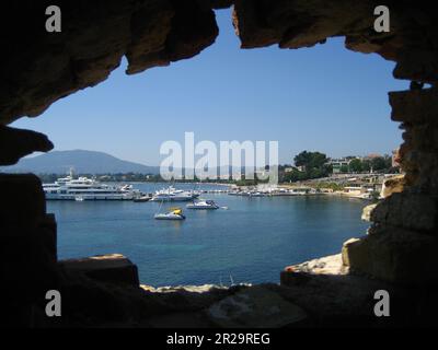 Yachts are docked on a Pier on a sunny summer day in Corfu and are seen through a hold in the wall. Stock Photo