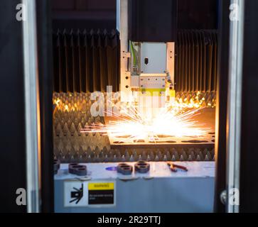 CNC fiber laser cutting machine cutting metal sheet with flying sparks. Industrial metalworking manufacturing. Stock Photo