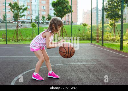 A girl on the playground with a ball plays basketball. Outdoor city basketball court Stock Photo