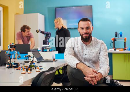 A man sitting in a robotics laboratory while his colleagues in the