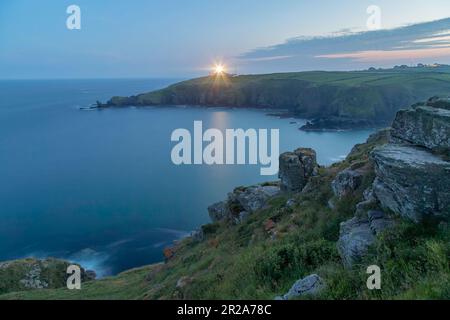 Looking across Housel Bay towards a lit Lizard Point lighthouse at dusk on the north Cornwall coast Stock Photo