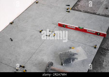 The process of laying tiles on the floor using tools and fixtures. Gray tiles. Room renovation Stock Photo