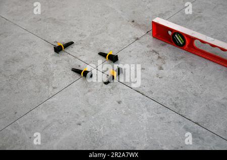 The process of laying tiles on the floor using tools and fixtures. Gray tiles. Room renovation Stock Photo