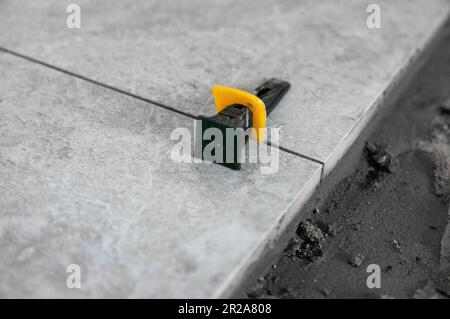 The process of laying tiles on the floor using tools and fixtures. Gray tiles. Room renovation Stock Photo