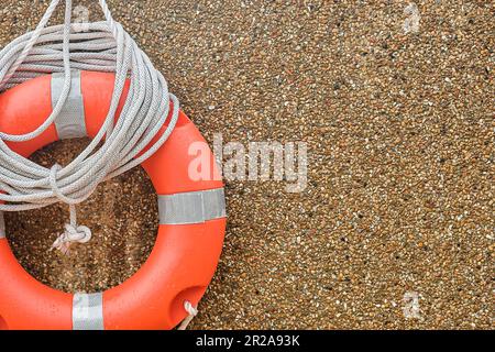 Orange lifebuoy and white rope hanging on gravel wall, copy space for text. Stock Photo