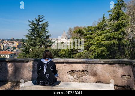 Rom, Italien, März 2023 Eine Frau auf einer Bank sitzend genießt den Blick vom Gianicolo Hügel auf den Vatikan und die Peterskirche Stock Photo