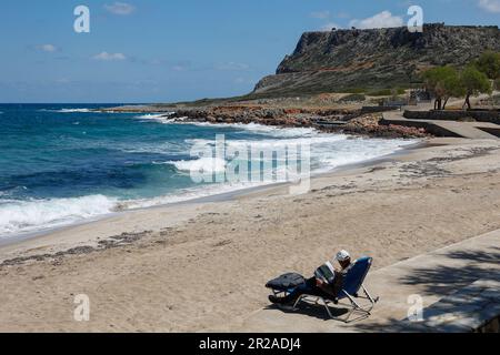 Senior man  relaxing while sitting on folding chairs at beach reading a magazine,Kalimera Kriti beach,Sissi, Crete,Greece Stock Photo