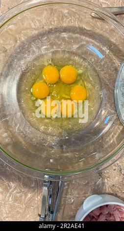 Overhead view of six raw eggs with unbroken yolk in a clear bowl on a kitchen counter. Stock Photo