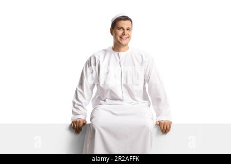 Young man in ethnic wear sitting on a white panel isolated on white background Stock Photo