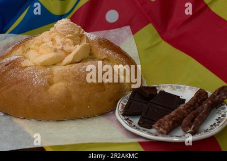 Close-up of a mona pascua next to chocolate and dry Easter sausages, typical Easter foods in Valencia (Spain) with the flag of the Valencian Community Stock Photo