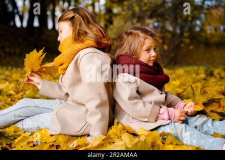 Beautiful little girls in bright yellow red orange autumn warm knitted scarf snood with head wreath of maple leaves,foliage walking in forest. Fun pla Stock Photo