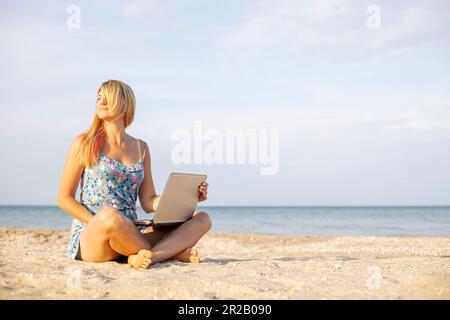 Beautiful woman with laptop computer on the beach. Working remotely on seashore Stock Photo