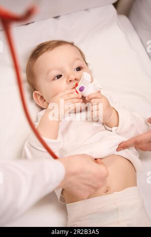 Child lying in cot being examined by neonatologist with stethoscope Stock Photo