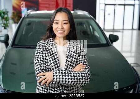 Long-haired brunette stands in front of a sparkling new car Stock Photo