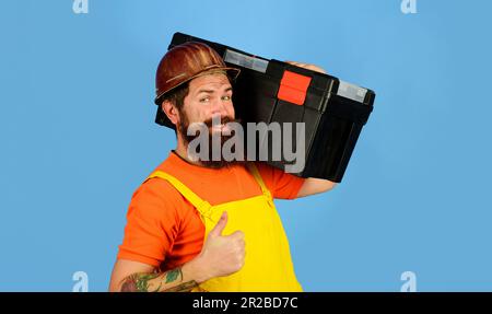 Repair. Repairman in overalls and safety helmet with toolbox showing thumb up. Man with toolbox. Builder in uniform with tool box for repair. Handyman Stock Photo