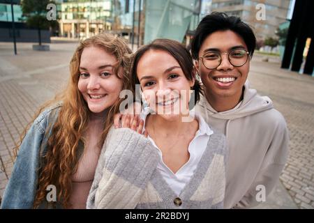 Portrait of three smiling multiracial young college students. Classmates cheerful and united. Stock Photo
