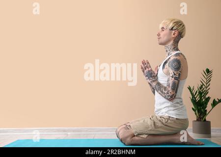 Tattooed young man meditating near beige wall Stock Photo