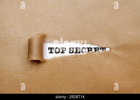 Brown paper torn revealing behind a white paper with "Top Secret" written on it. Stock Photo