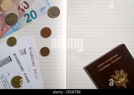 Some euro coins and banknotes as well as a french passport and 2 boarding pass on the top of an opened notebook. Stock Photo