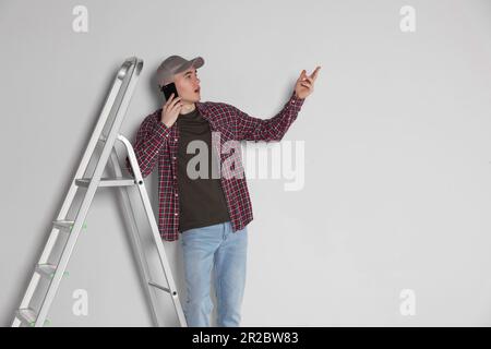 Emotional handyman talking on phone near stepladder in room Stock Photo