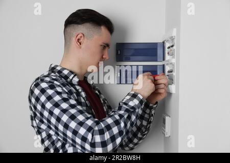 Young handyman with screwdriver repairing electrical panel board indoors Stock Photo