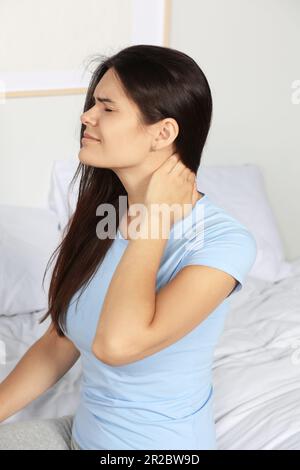 Young woman suffering from neck pain on bed in bedroom Stock Photo