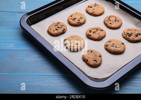 Baking pan with parchment paper and tasty cookies on light blue wooden table Stock Photo