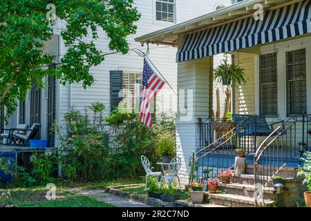 NEW ORLEANS, LA, USA - MARCH 14, 2023: American flag hanging from a front porch with a porch swing at a home in Uptown New Orleans, LA, USA Stock Photo