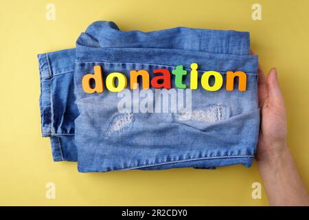 Clothes and an inscription: the donation is on it. Symbol of charity, yellow background Stock Photo