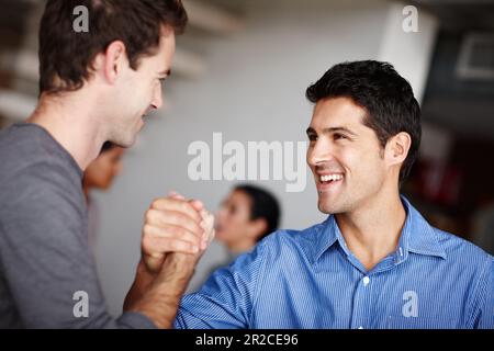 Motivating one another to success. Two business colleagues clasping hands and laughing in the office. Stock Photo