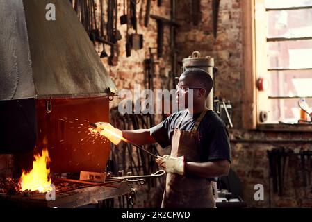 Blacksmith, fire and a black man welding metal in a workshop for manufacturing or industrial design. Factory, melting or industry with a male welder Stock Photo