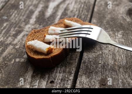 a piece of black bread with bacon and a fork on a wooden table for lunch Stock Photo