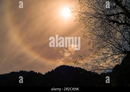 Scenic beautiful sun halo phenomenon in Himalayan range, Uttarakhand, India. Lens flare effects on golden suns with Light particles and rainbow halo. Stock Photo