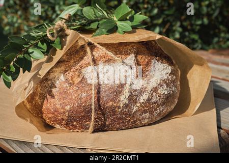 Close-up of traditional round bread on craft paper package decorated with branch at Christmas market. Stock Photo