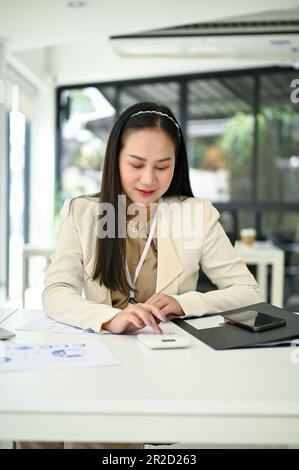 Portrait of a professional and focused millennial Asian businesswoman or female accountant using a calculator to recheck financial data and analyzing Stock Photo